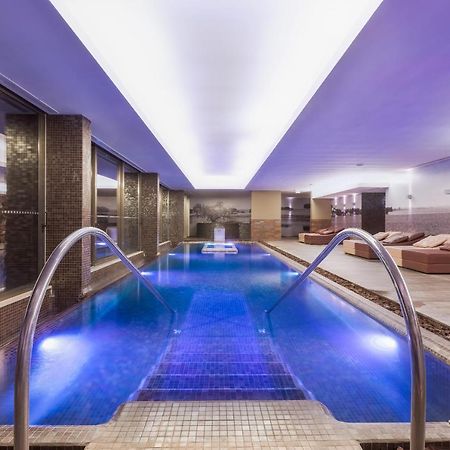 Ap Lago Montargil - Conference & Spa Exterior foto The photo shows a modern indoor swimming pool area. The pool features a sleek design with steps leading into the water and a gentle curve at the sides. The water is illuminated in a blue hue, enhancing the relaxing atmosphere. Surrounding the pool ar