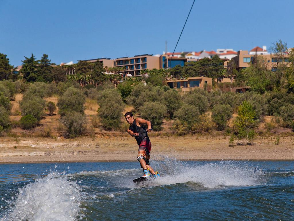 Ap Lago Montargil - Conference & Spa Exterior foto The photo shows a person wakeboarding on a body of water. The individual is being pulled by a cable, which is likely connected to a boat or a winch. The person is wearing a life jacket and swim shorts, balancing on the board as they enjoy the activit