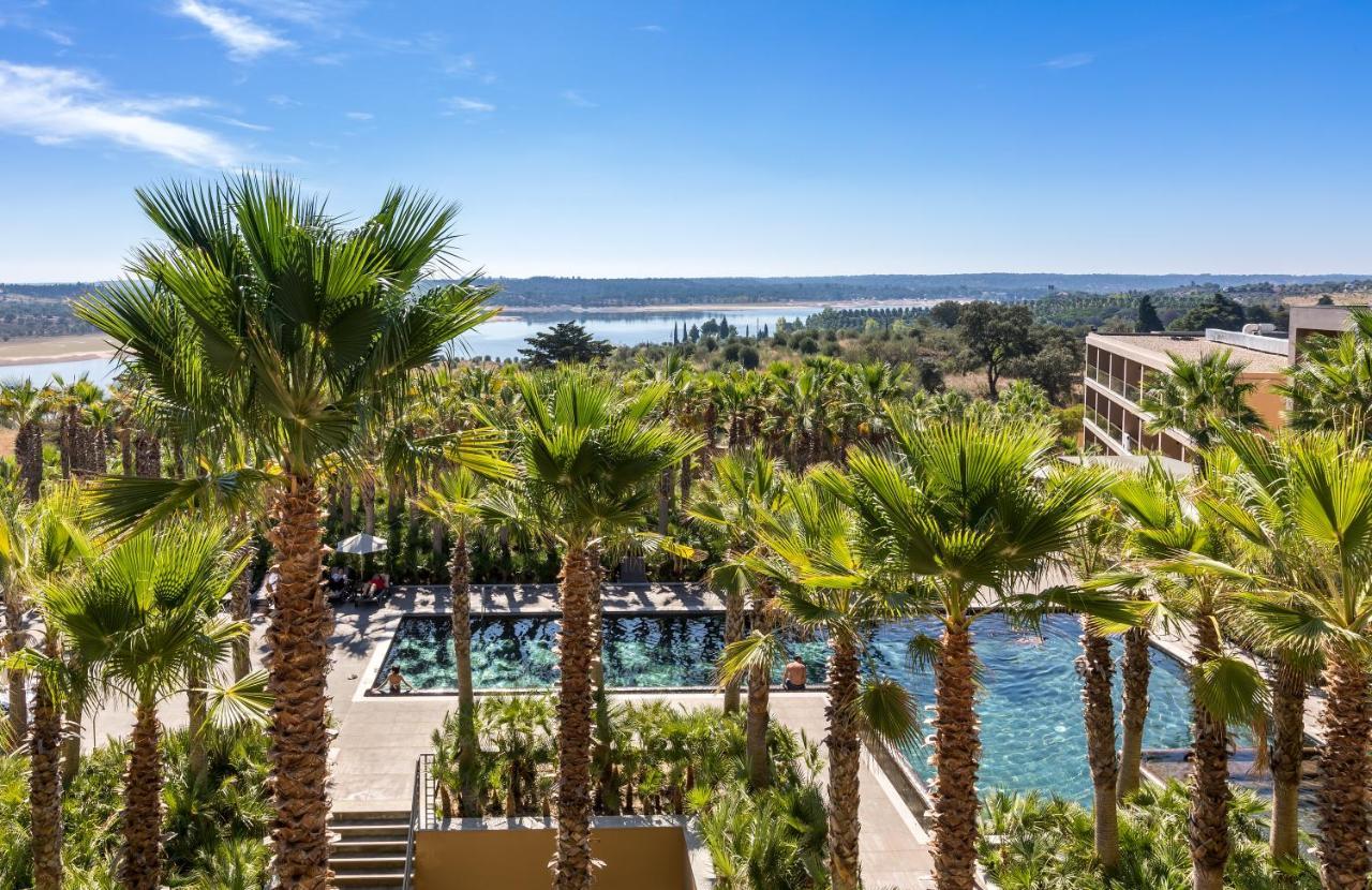 Ap Lago Montargil - Conference & Spa Exterior foto The photo depicts a picturesque resort landscape with a clear blue sky. In the foreground, there are tall palm trees surrounding a swimming pool area. The swimming pool has a modern design and is surrounded by lush greenery. In the background, you ca