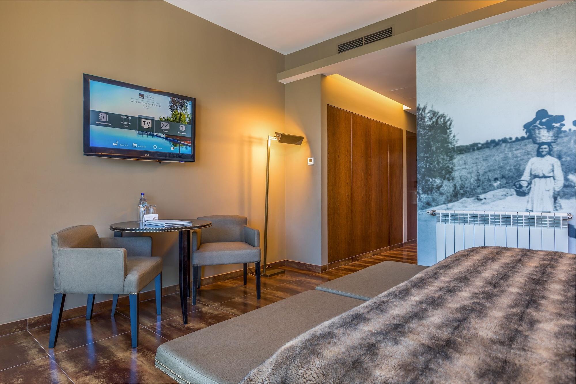 Ap Lago Montargil - Conference & Spa Exterior foto The photo shows an interior of a room, likely a hotel or a modern living space. In the foreground, there is a bed with a textured brown blanket. To one side, there are two comfortable chairs and a small table, possibly with a bottle of water. A flat-
