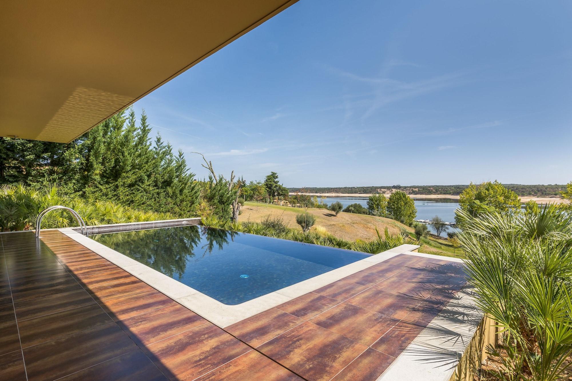 Ap Lago Montargil - Conference & Spa Exterior foto The photo shows a luxurious infinity pool situated on a terrace or deck. The pool features a sleek, modern design with a dark blue surface that reflects the surrounding scenery. In the background, there is a landscape of rolling hills and a body of w