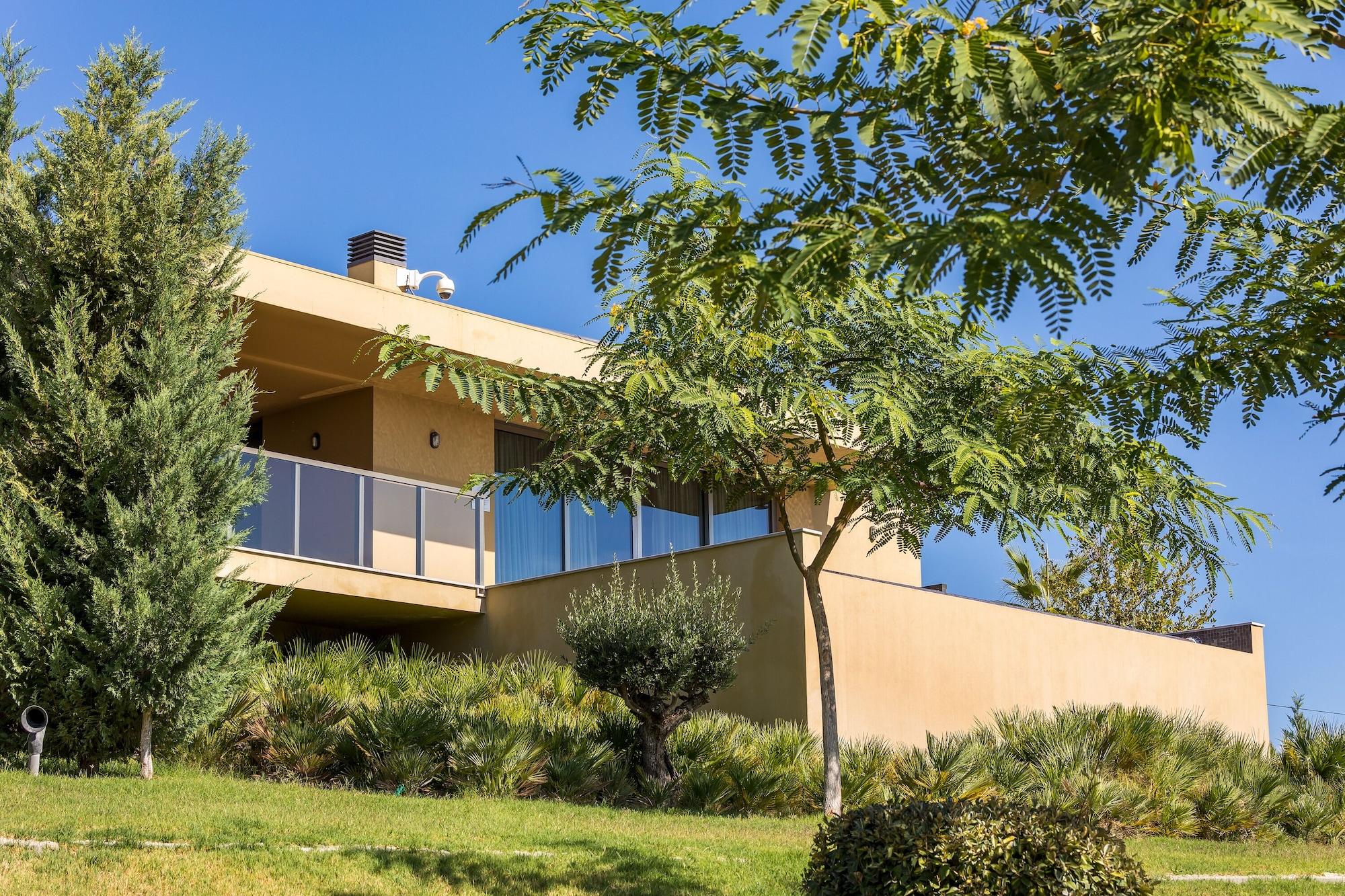 Ap Lago Montargil - Conference & Spa Exterior foto The photo showcases a modern house situated on a grassy slope. The house features a light-colored exterior with large windows and a balcony. Surrounding the building are several trees and landscaping that enhances the natural environment. The sky is 