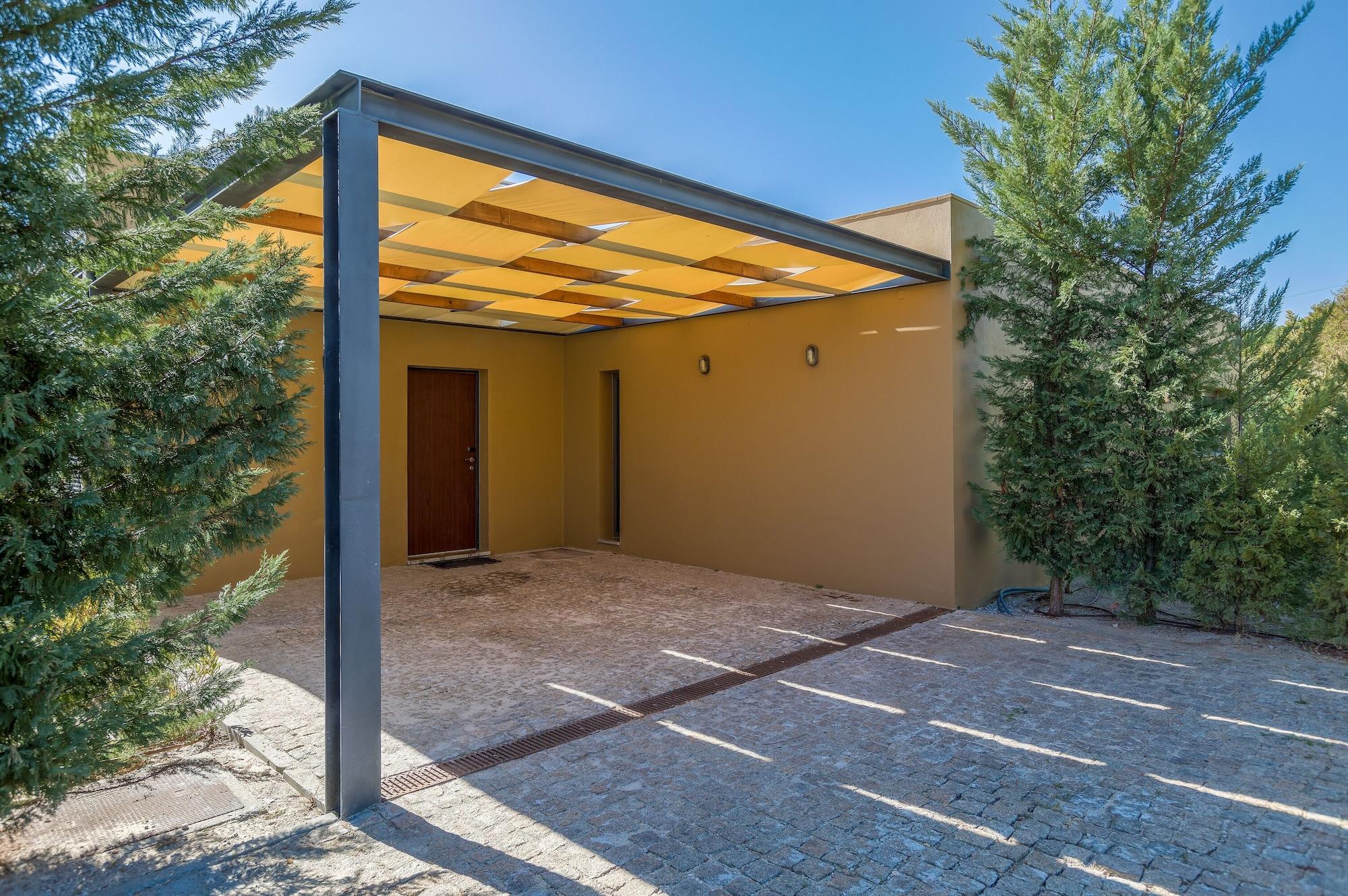 Ap Lago Montargil - Conference & Spa Exterior foto The photo shows an exterior view of a modern structure with a carport. The carport has a sleek, metallic frame and a yellowish canopy above it. In front of the structure, there is a paved area made of stone or tiles. The main entrance features a wood