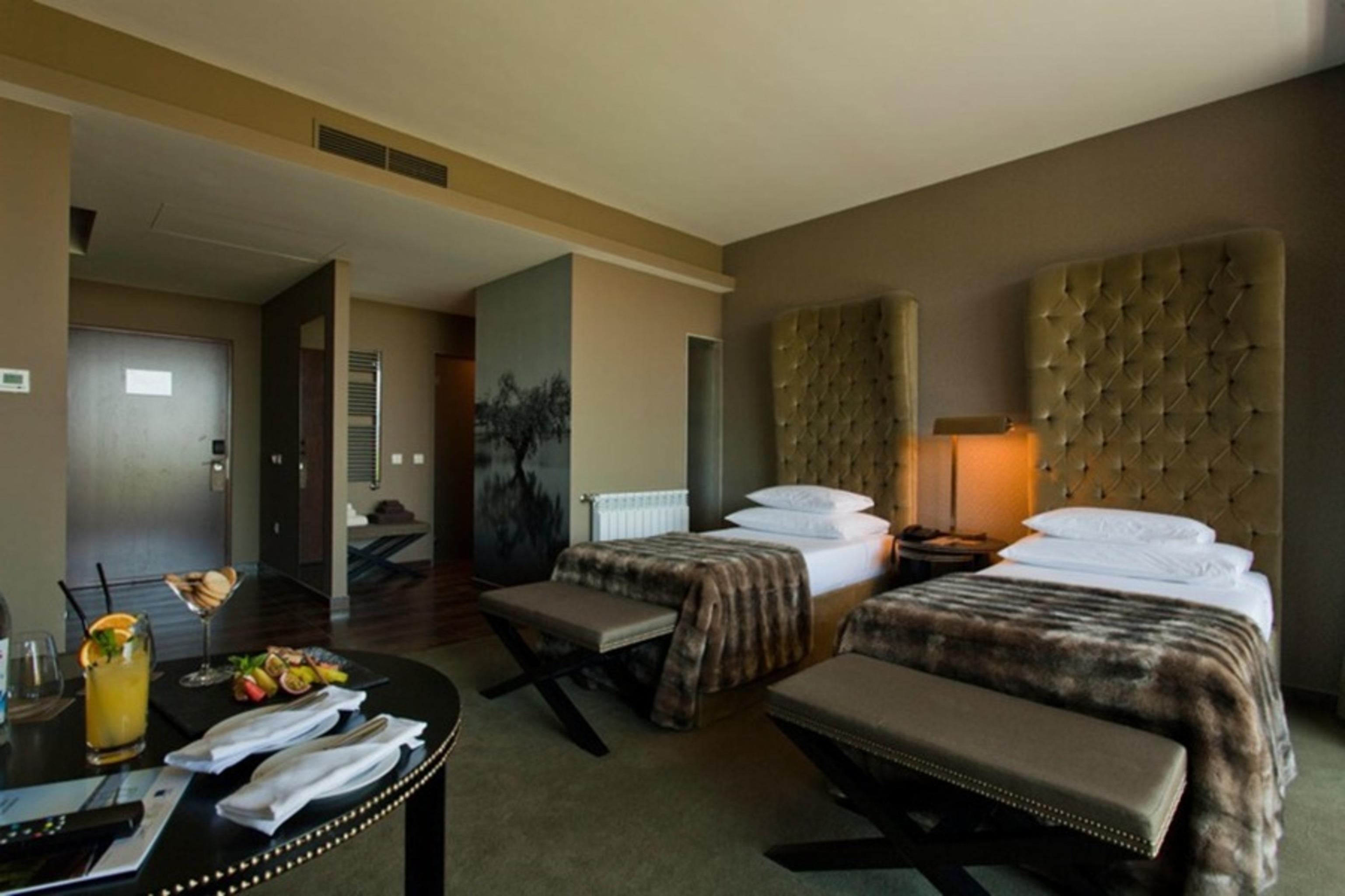 Ap Lago Montargil - Conference & Spa Exterior foto The photo shows a stylish hotel room featuring two beds with plush, upholstered headboards. The room has a modern and elegant design, with earthy tones dominating the decor. A small round table is set up in the foreground, displaying a drink and some