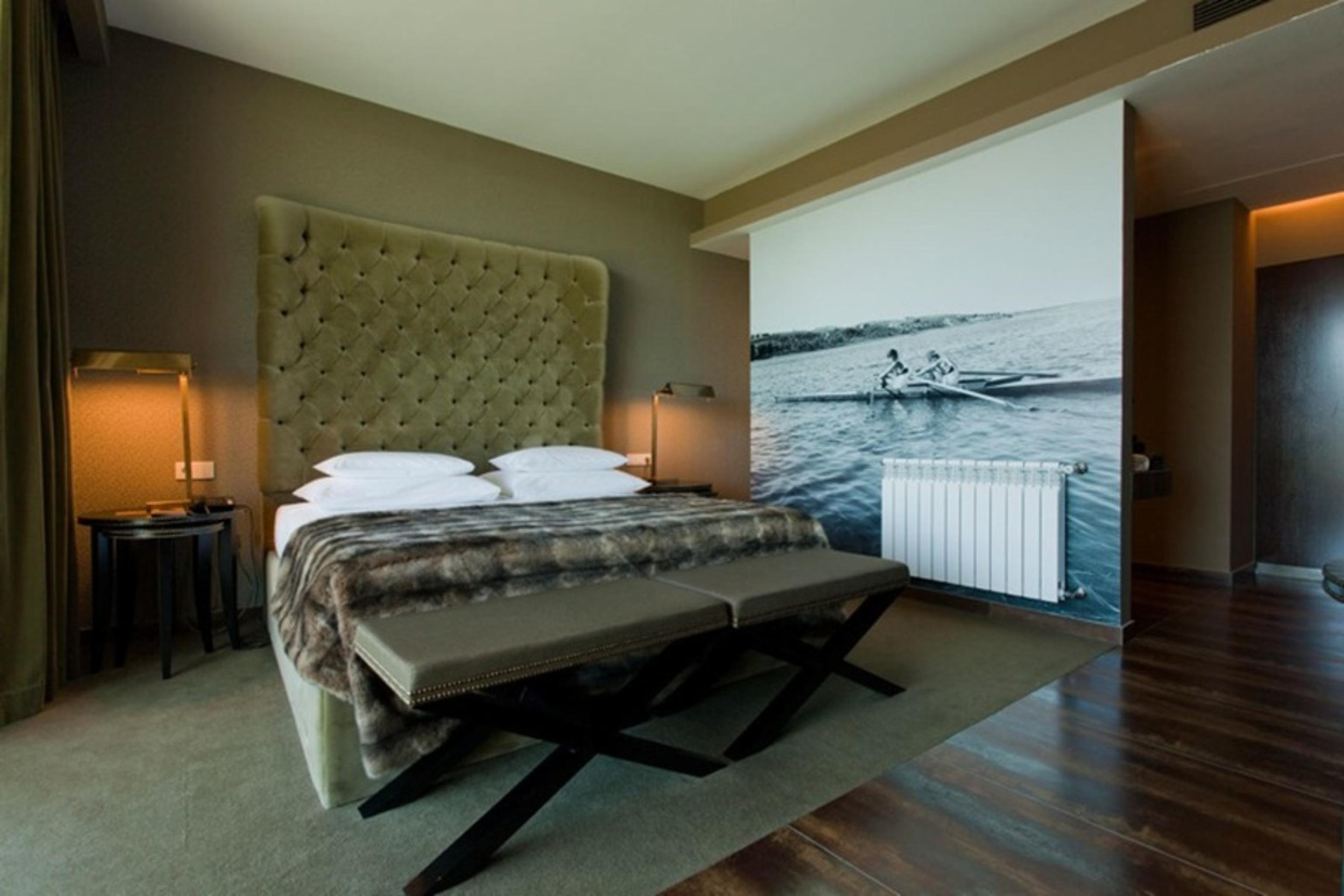 Ap Lago Montargil - Conference & Spa Exterior foto The photo shows a modern hotel room featuring a large bed with a tufted headboard and plush bedding. The color palette is neutral, with shades of green and gray. On one side of the room, there are bedside tables with lamps. A comfortable bench sits a