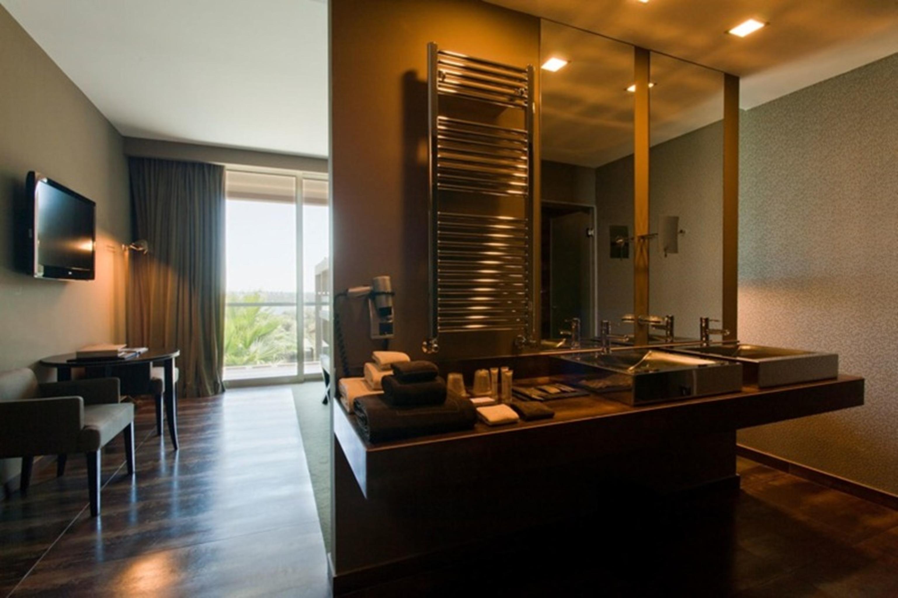 Ap Lago Montargil - Conference & Spa Exterior foto The photo displays a modern hotel room with a contemporary design. The room features a large window, allowing natural light to enter and offering a view outside. On one side, there is a sitting area with a small table and chairs. The other side showc