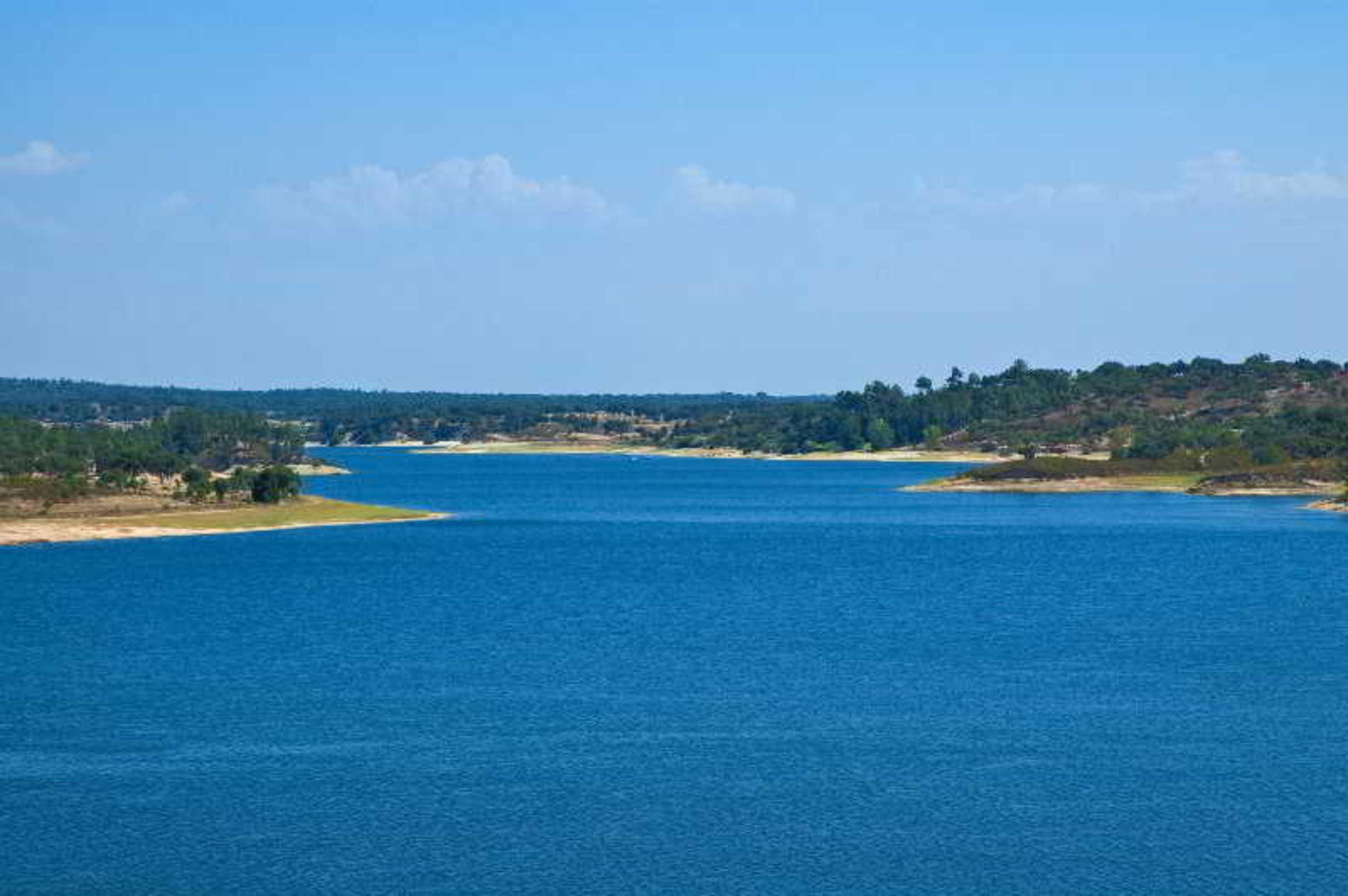 Ap Lago Montargil - Conference & Spa Exterior foto The photo depicts a serene landscape featuring a large body of water, likely a lake or river. The water appears calm and is reflecting a clear blue sky with some clouds. Surrounding the water, there are patches of green land and trees, indicating a n