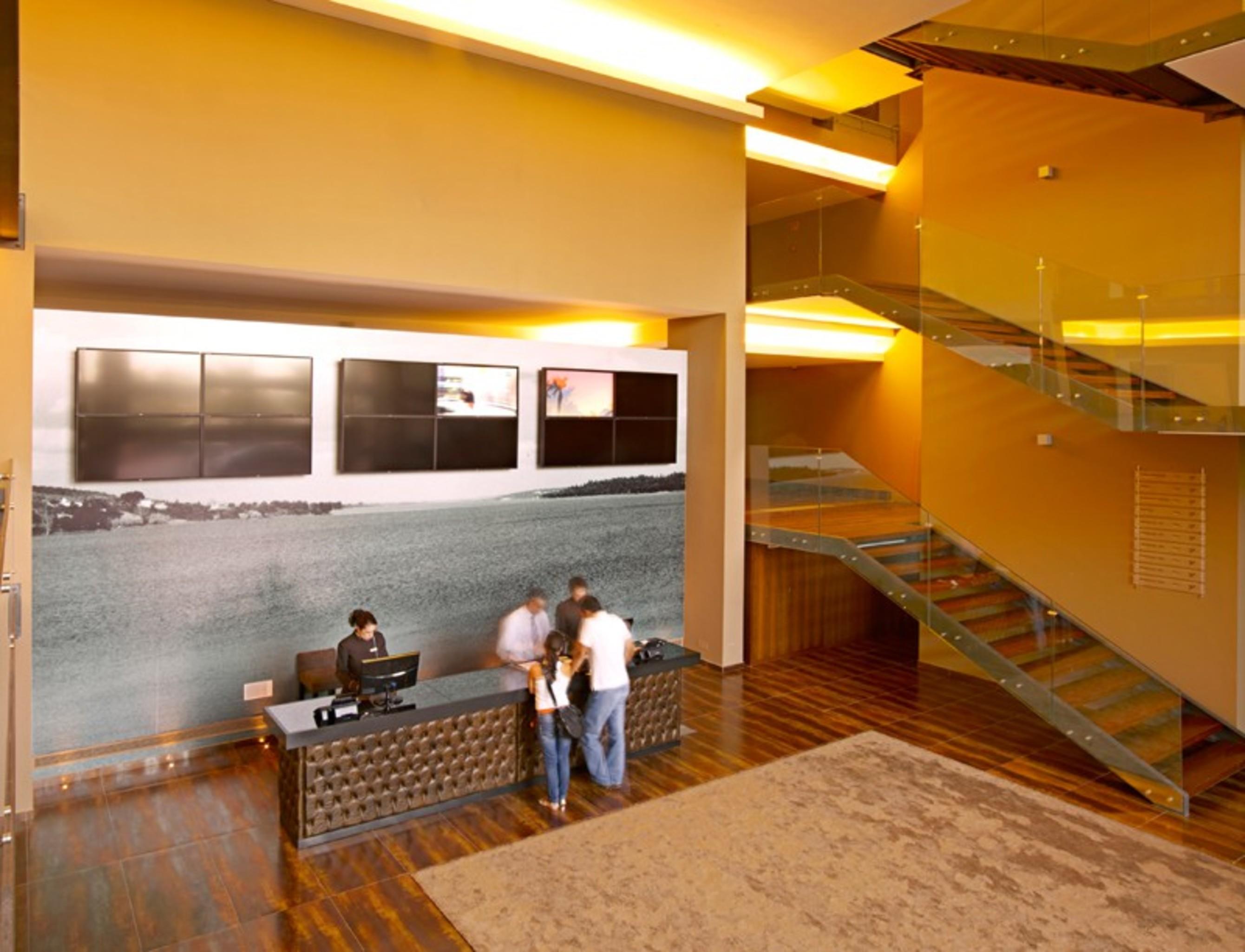 Ap Lago Montargil - Conference & Spa Exterior foto The photo depicts a modern lobby area with a reception desk. The design features a combination of warm colors and wood flooring. In the background, there is a large wall-mounted screen or display, showcasing several monitors. The wall behind the desk