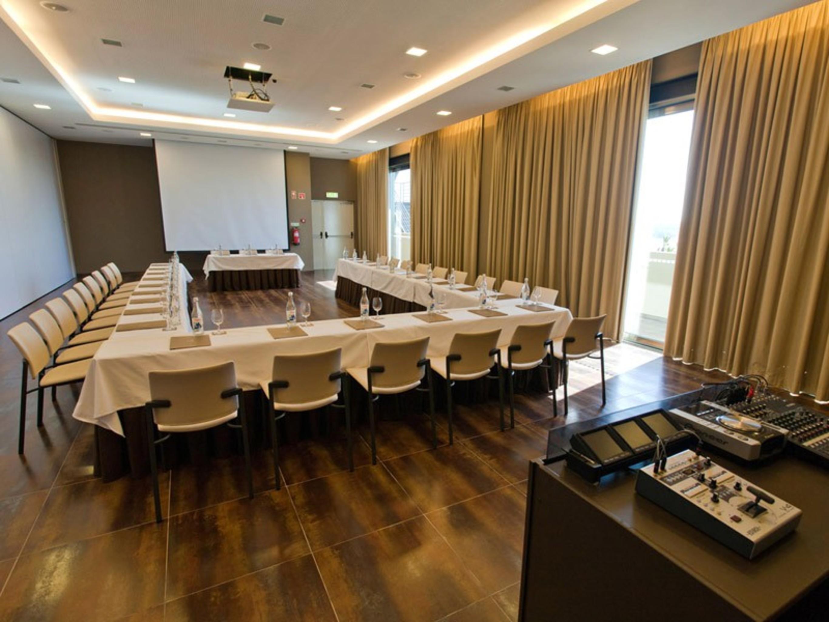 Ap Lago Montargil - Conference & Spa Exterior foto The photo shows a modern conference room set up for a meeting. There are several tables arranged in a U-shape, surrounded by chairs. A large screen and projector are positioned at the front, with a table for speakers or presenters. The room has large