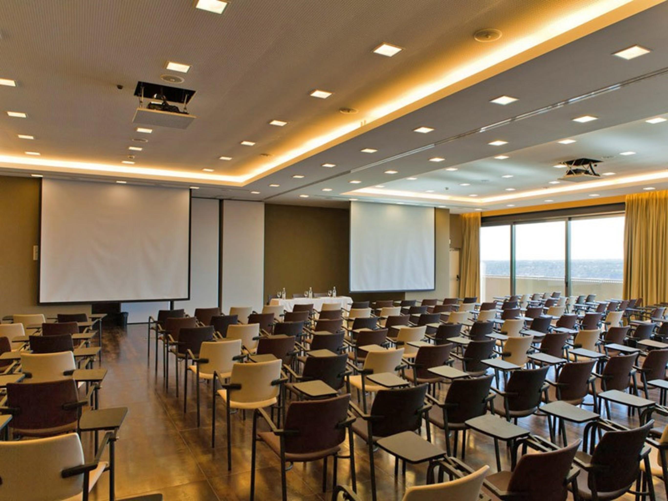 Ap Lago Montargil - Conference & Spa Exterior foto The photo shows a large conference room set up for a presentation or meeting. There are multiple rows of chairs arranged in a semi-theater style, facing two large projection screens. The room has a modern design, with soft lighting and large windows 