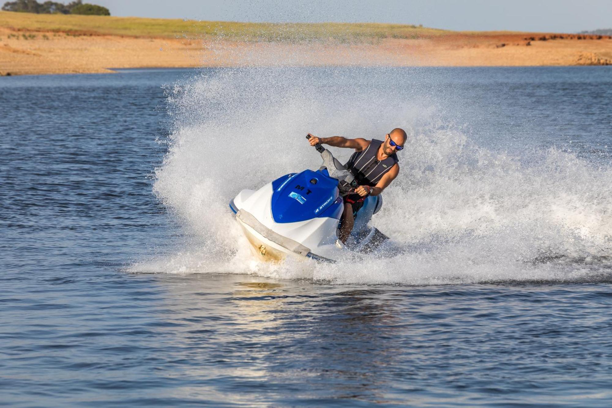 Ap Lago Montargil - Conference & Spa Exterior foto The photo shows a person riding a jet ski over a body of water. The rider is wearing sunglasses and a life vest, leaning forward as the jet ski accelerates, creating a spray of water around them. The background features a natural landscape, likely a 